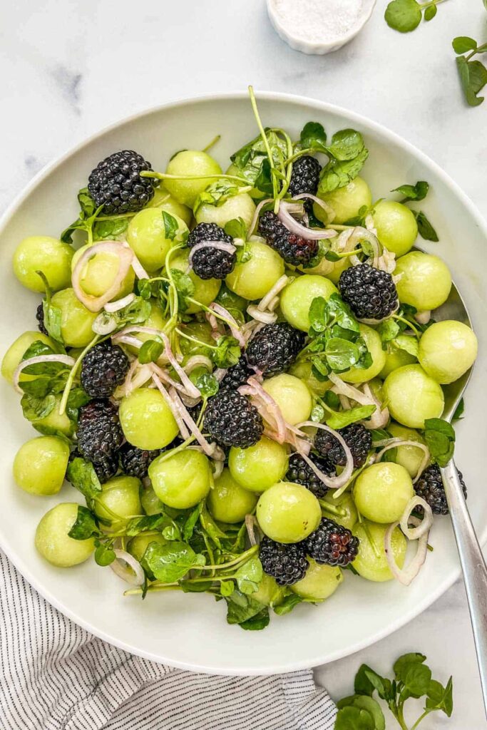 Salad with spinach, onion, honeydew balls, and blackberries .